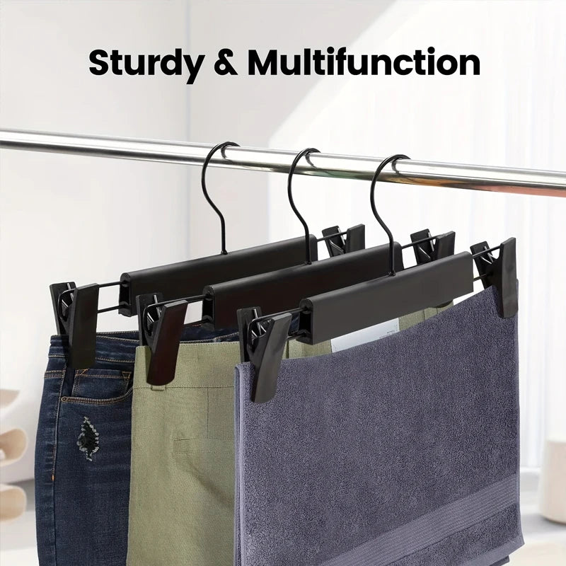 Black adjustable clip hangers holding denim and fabric garments on a rod.