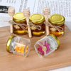 Hexagon mini glass honey jars with wood dippers and gold lids displayed on a wooden board.