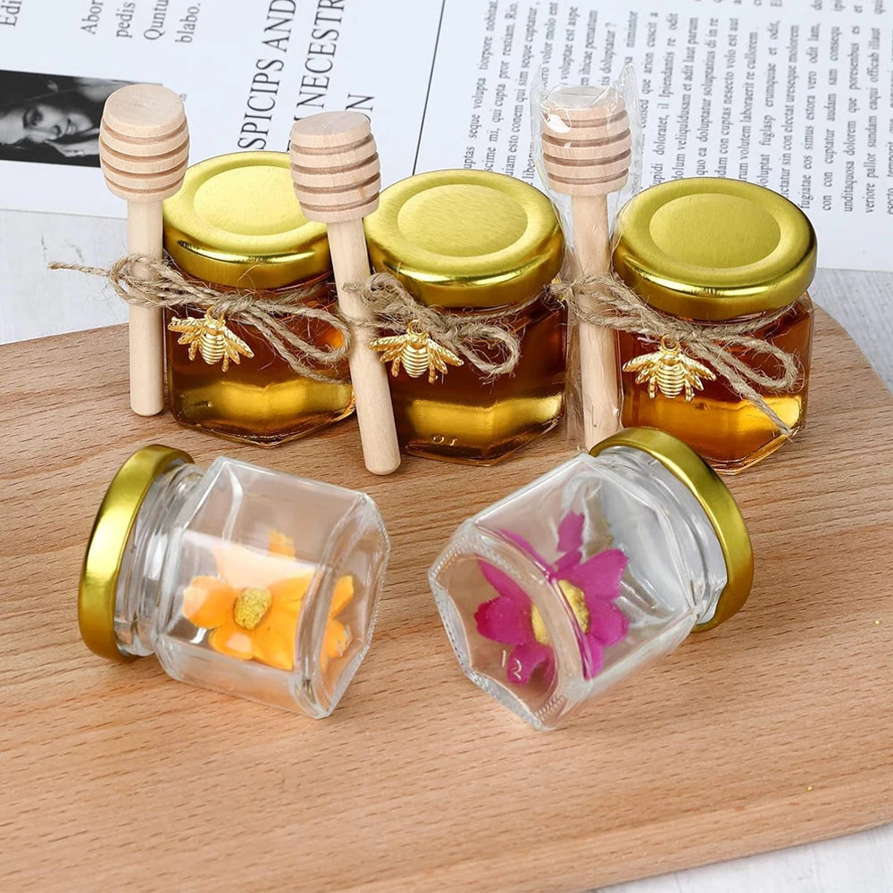 Hexagon mini glass honey jars with wood dippers and gold lids displayed on a wooden board.