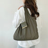 A person is holding a olive green retractable keychain tote bag with a gold accent, folded and ready for use.