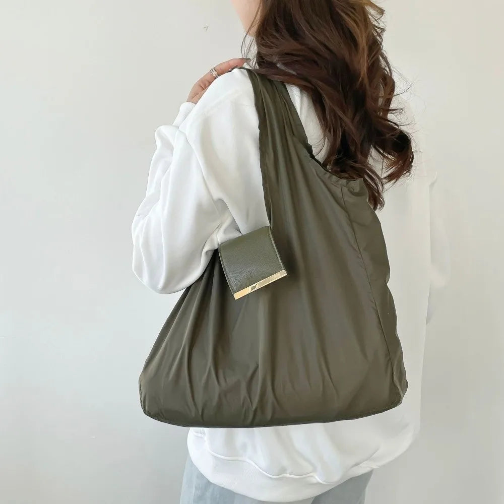 A person is holding a olive green retractable keychain tote bag with a gold accent, folded and ready for use.