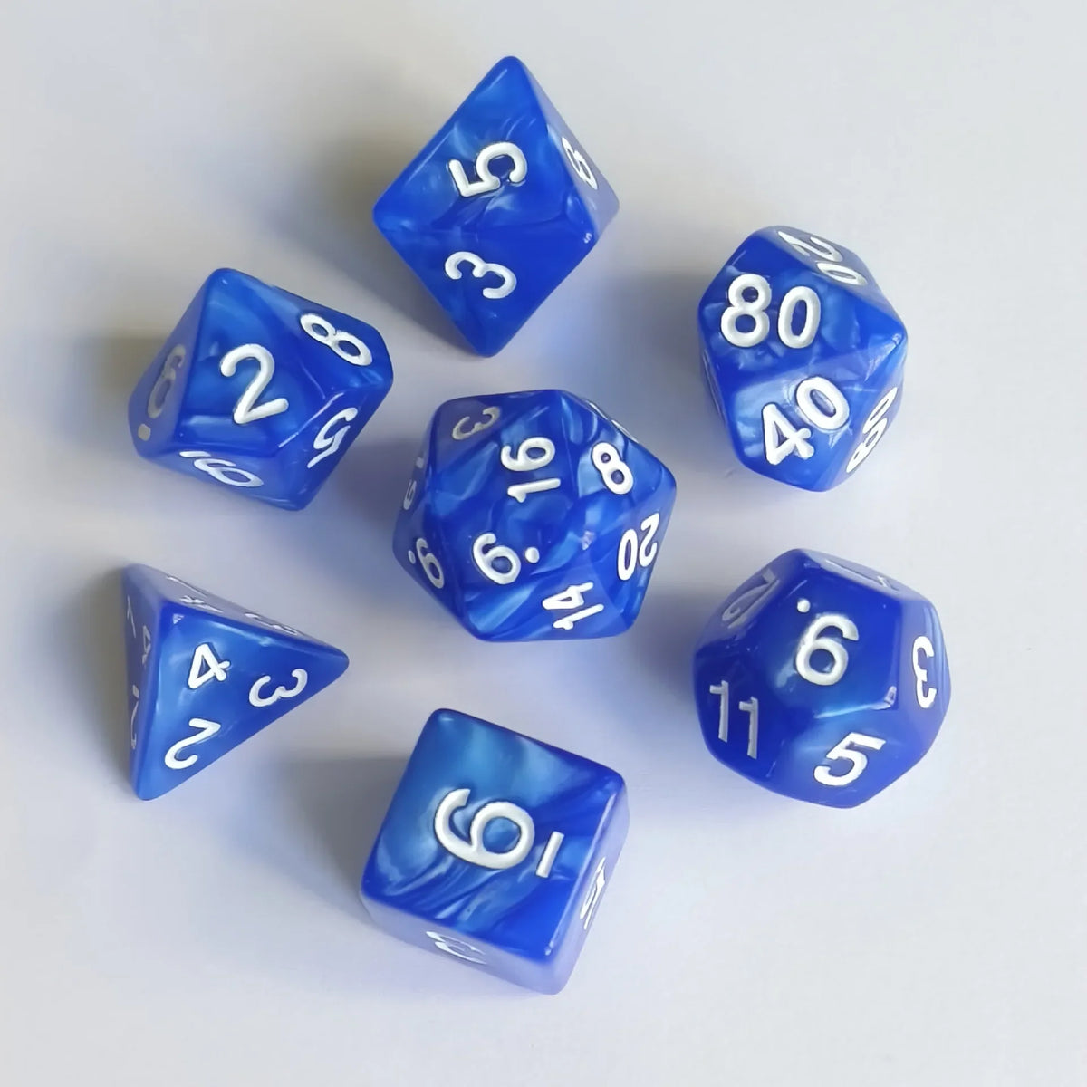 A collection of seven blue translucent polyhedral dice scattered on a white surface.