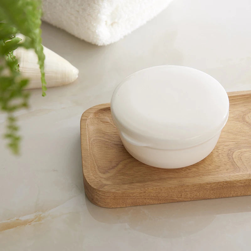 A white sealed portable soap box with a drainage cover rests on a wooden tray next to a green plant.