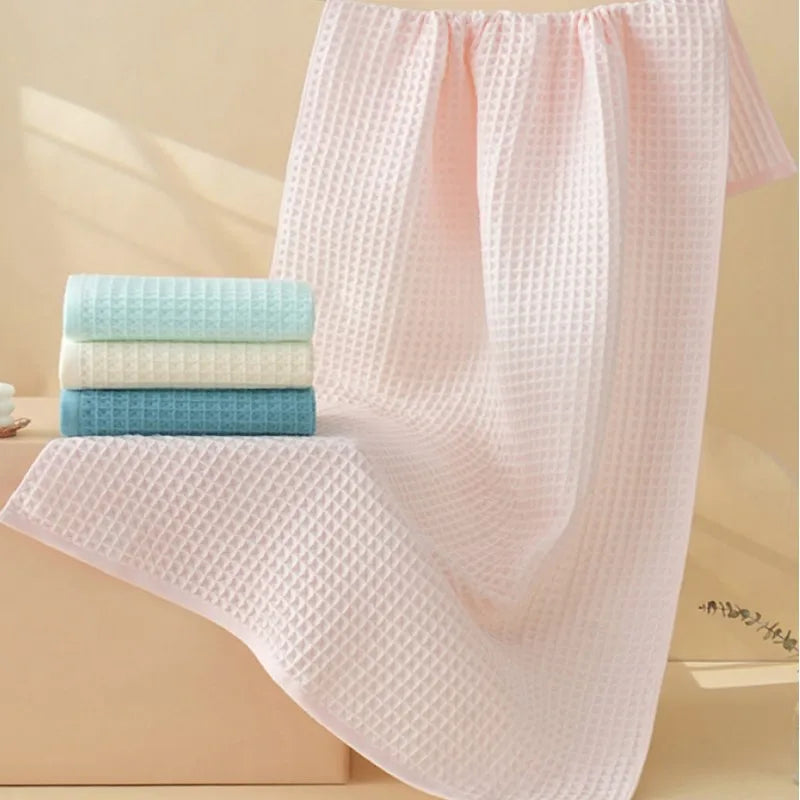 Pink waffle weave bath towels stacked on a light wood surface.