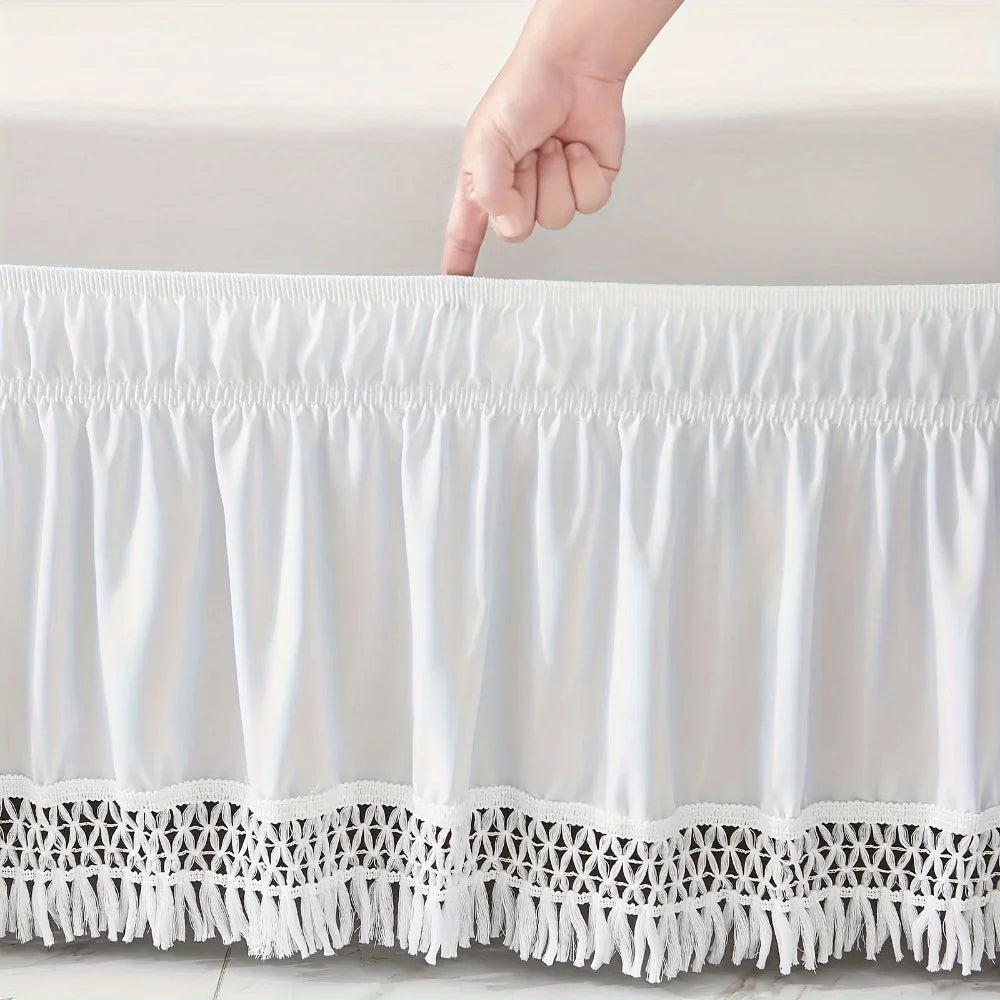 White elastic wrap-around ruffled bed skirt with lace trim being touched by a hand.