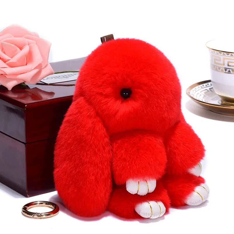 A fluffy red angel bunny keychain with a pom pom tail resting on a dark box.