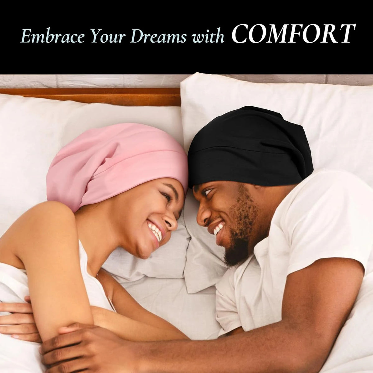 A smiling couple wearing silk satin sleep bonnets while relaxing in bed.