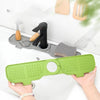 A hand holds a green silicone sink faucet mat with a rotatable splash guard next to a black faucet.