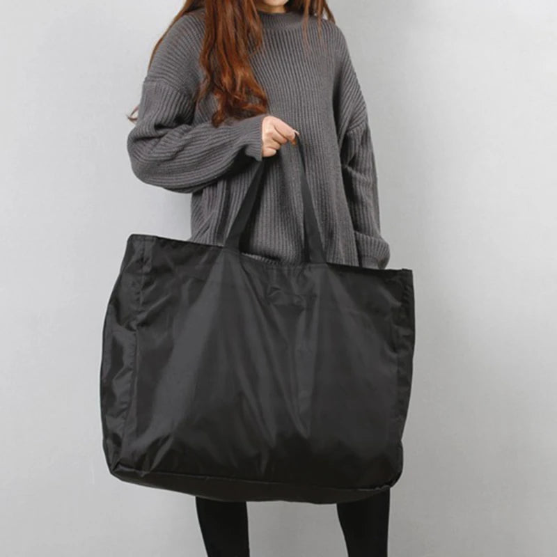 A person wearing a gray sweater is holding a black reusable large-capacity grocery tote.