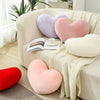 A set of heart-shaped plush throw pillows in shades of pink, purple, and cream resting on a light-colored sofa.