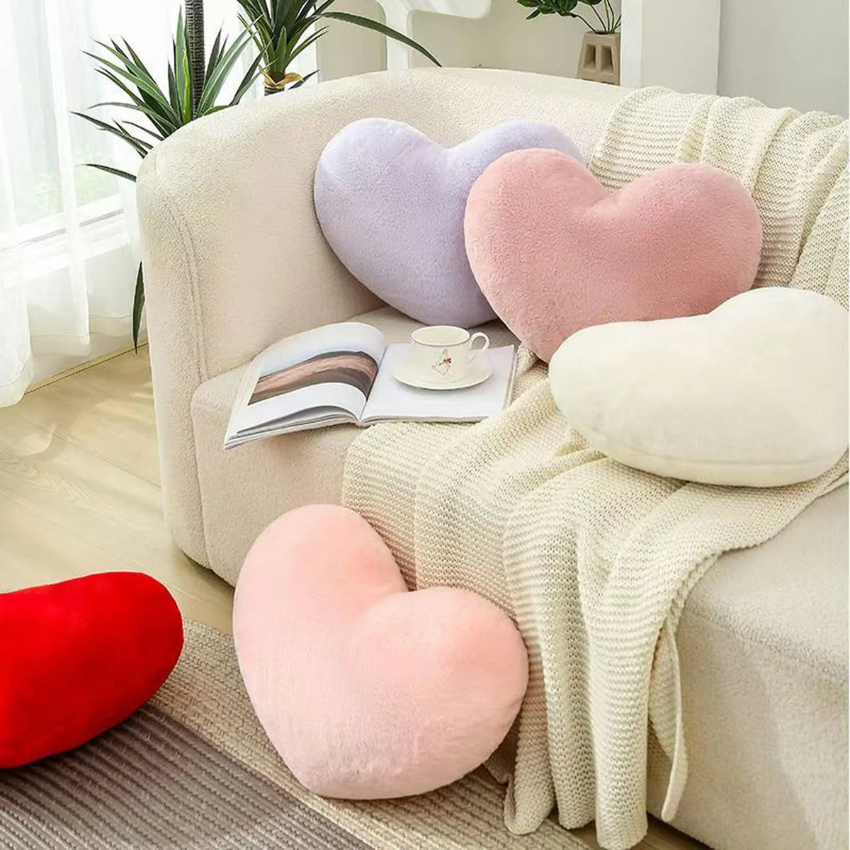 A set of heart-shaped plush throw pillows in shades of pink, purple, and cream resting on a light-colored sofa.
