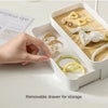 A white jewelry display rack with a removable drawer and wooden base, showing various gold and pearl jewelry pieces.