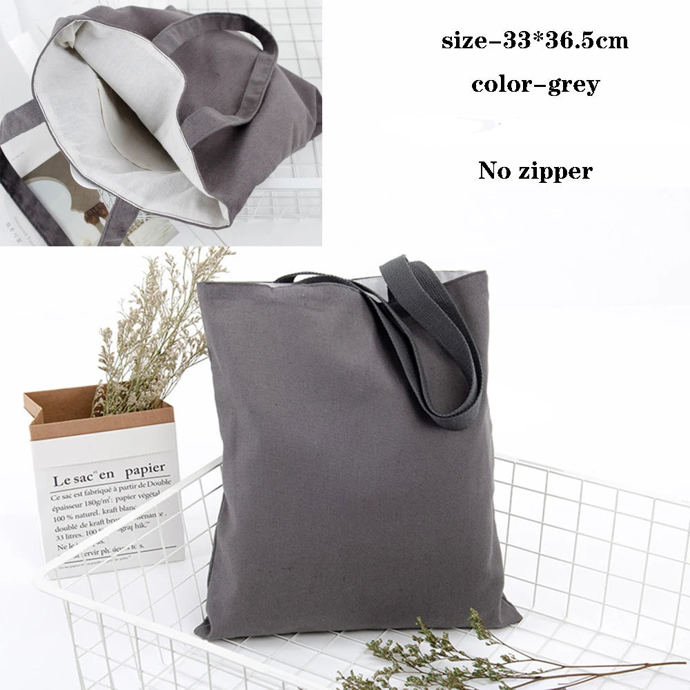 A grey foldable canvas tote bag shown next to a paper bag and some greenery.