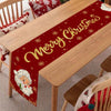 A festive red table runner with gold sparkling text reads Merry Christmas and features scattered gold snowflakes on a wooden 