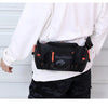 A black tactical chest bag worn by a person, featuring orange accents, is shown against a light background.