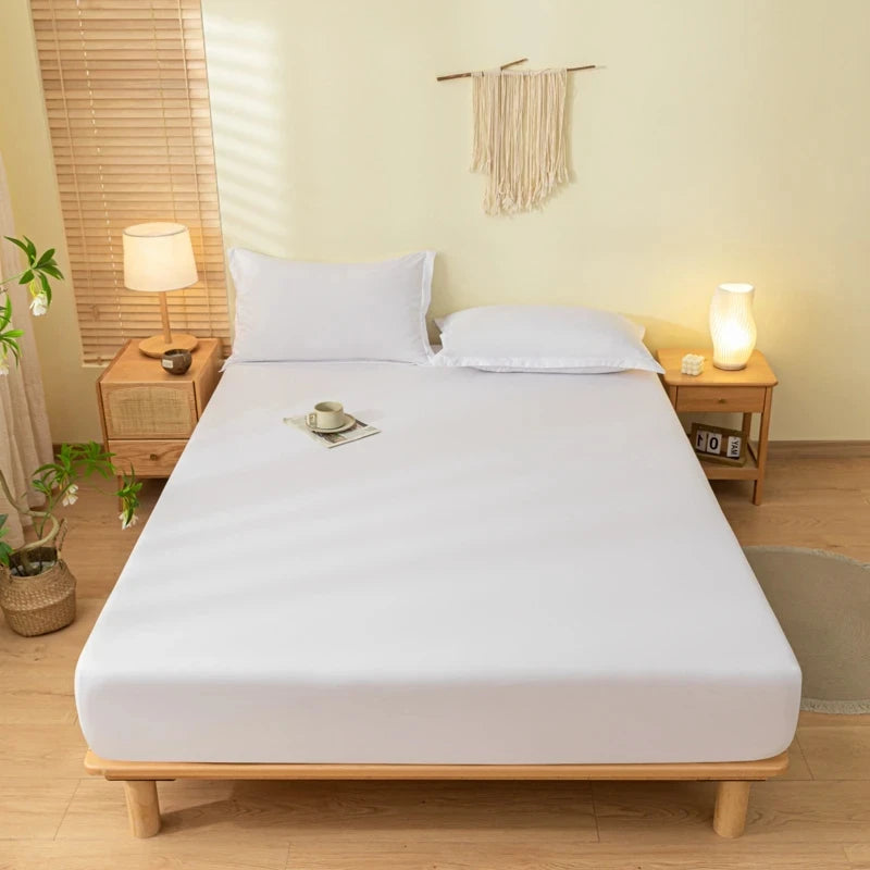 A white fitted bed sheet set with pillowcases is displayed on a wooden bed frame in a bright bedroom.