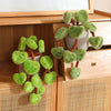 A potted plant decoration featuring lifelike green faux pothos leaves on woody stems, displayed in a wooden cabinet.