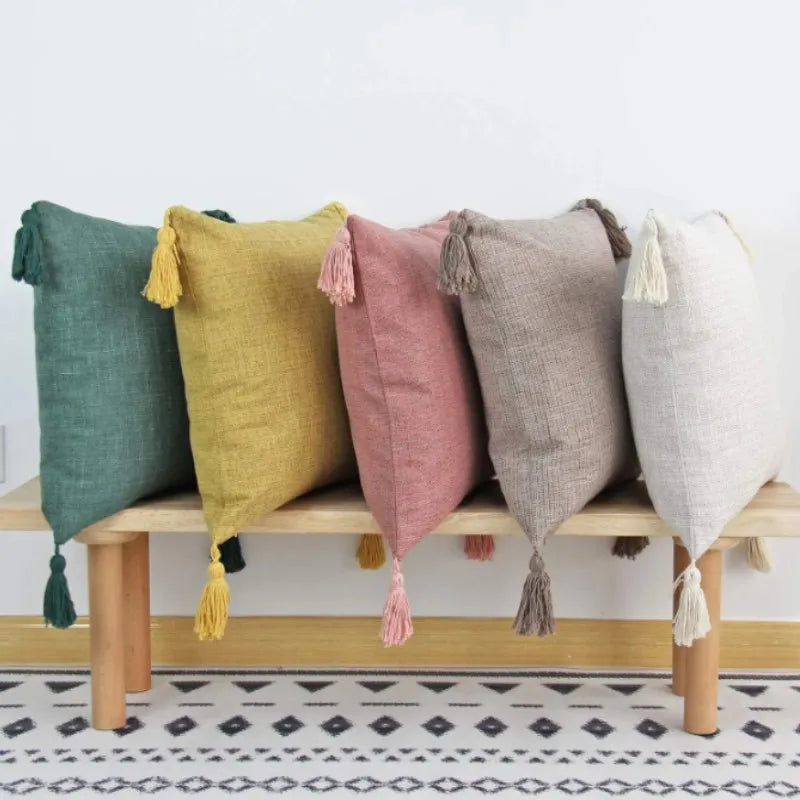 A row of nine cotton linen throw pillow covers in various muted colors like sage green, mustard yellow, pink, and gray with t