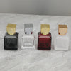 Four glass perfume bottles in various colors and finishes with gold-colored sprayers displayed on a light surface.