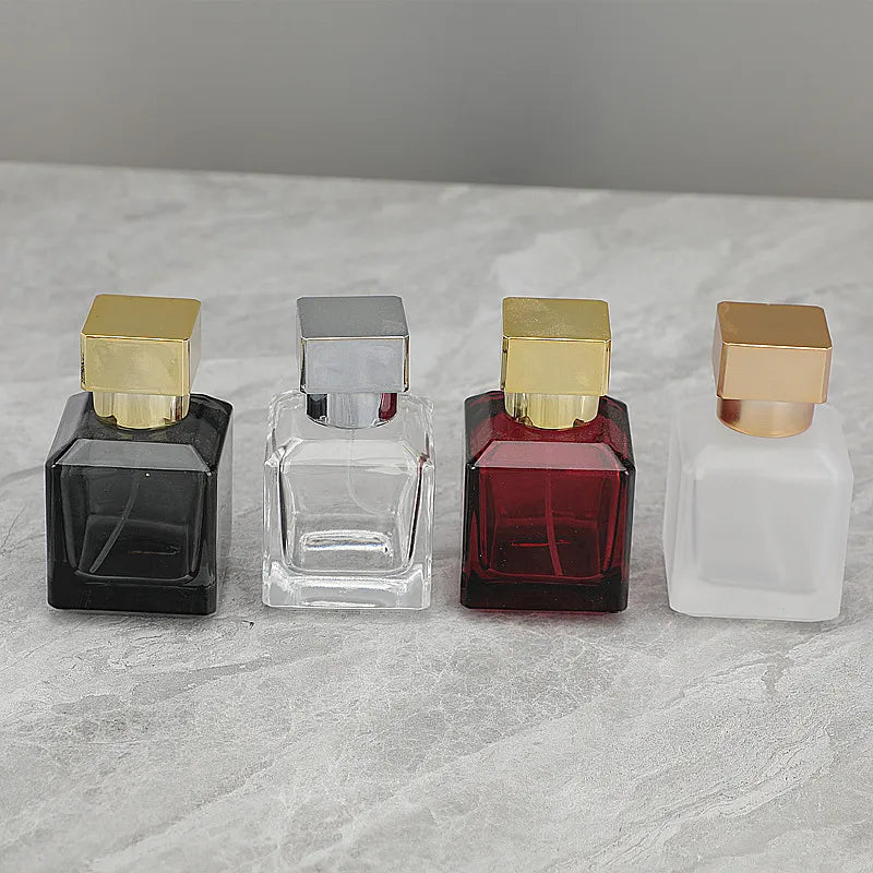 Four glass perfume bottles in various colors and finishes with gold-colored sprayers displayed on a light surface.