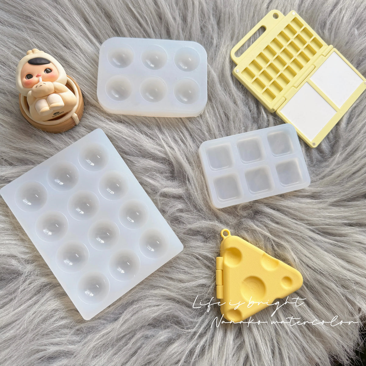 A collection of silicone paint palette trays in white and yellow on a gray fluffy surface.