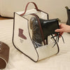 A beige storage bag with a transparent window holds a black boot and is being held by a hand.