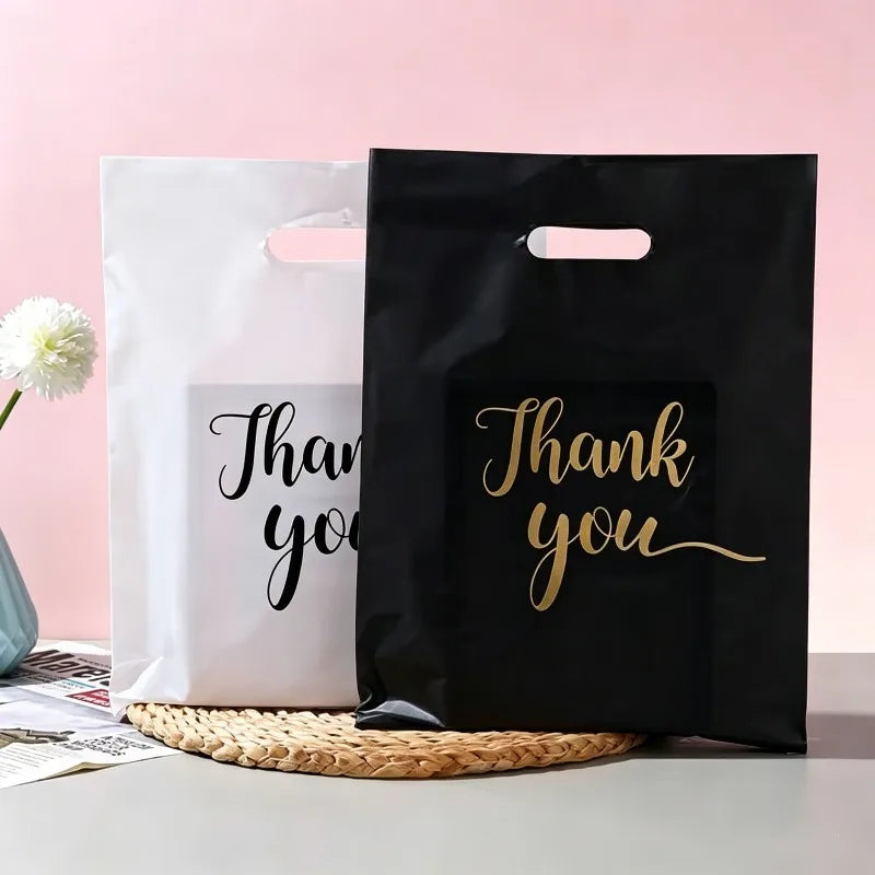 Two gift bags, one white and one black, featuring gold script text that reads Thank you.