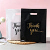Two gift bags, one white and one black, featuring gold script text that reads Thank you.