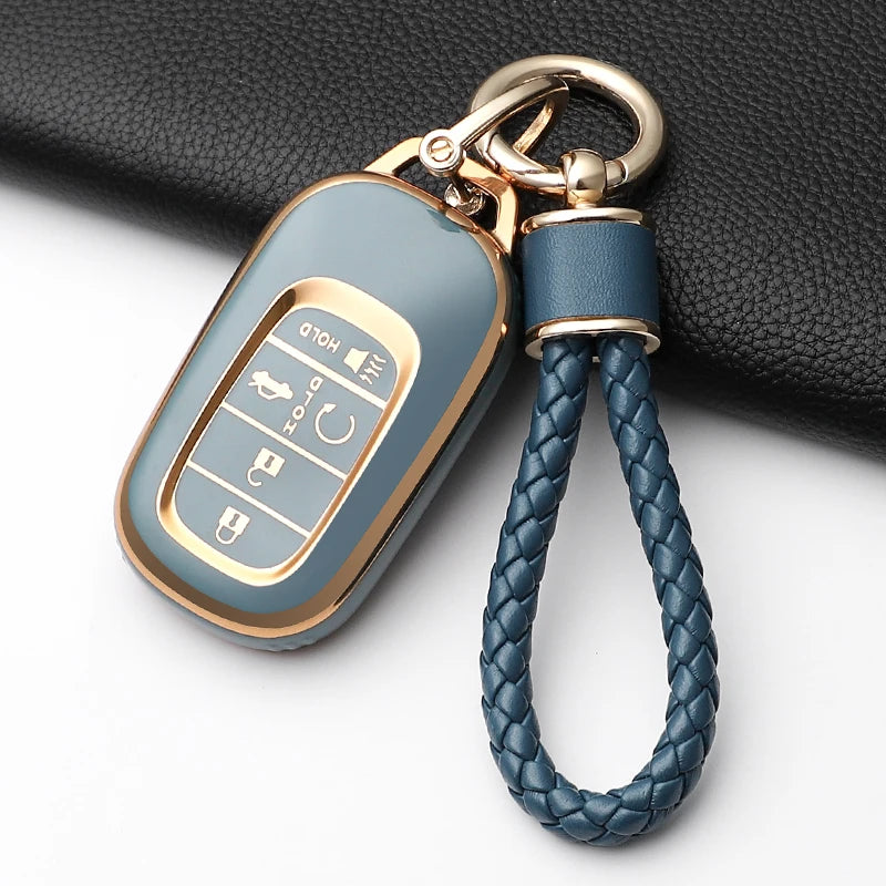 A light blue Honda key fob cover with a gold-toned chain attached to a black leather background.