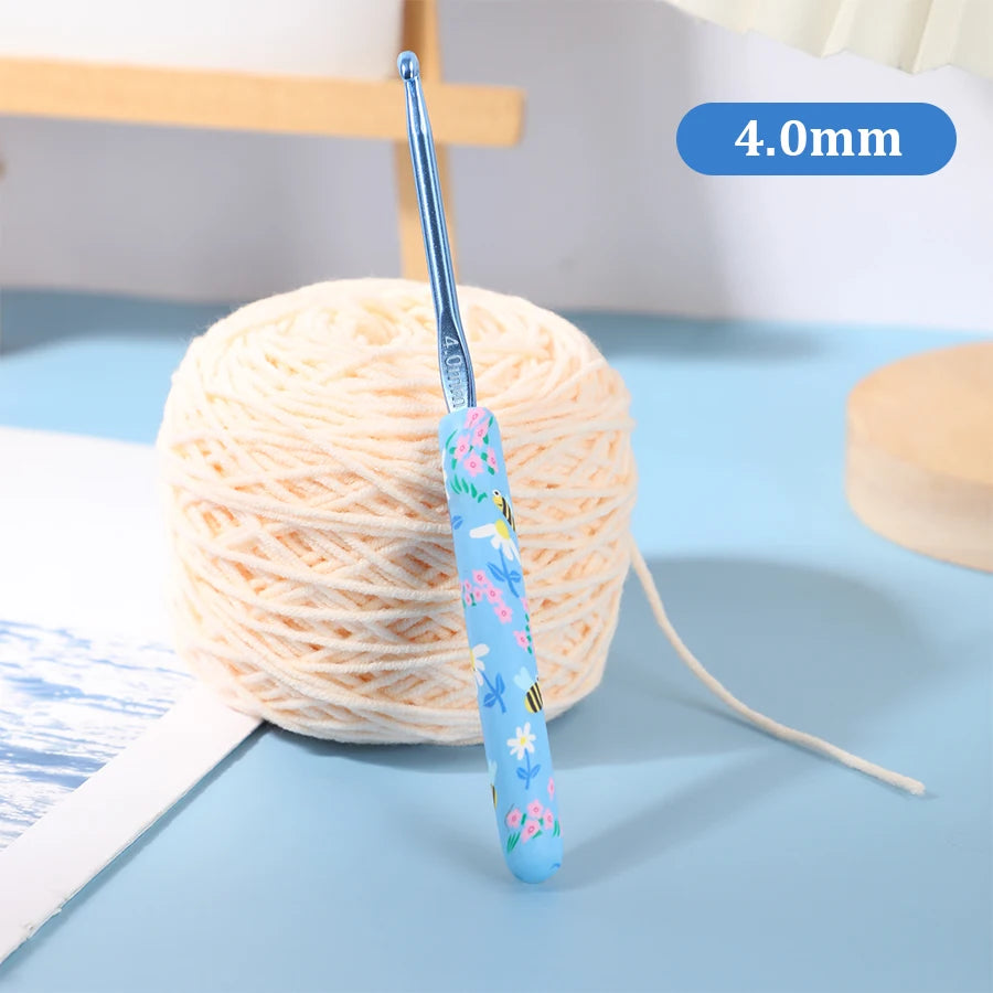 A blue crochet hook with a bee design is shown next to a ball of light-colored yarn.