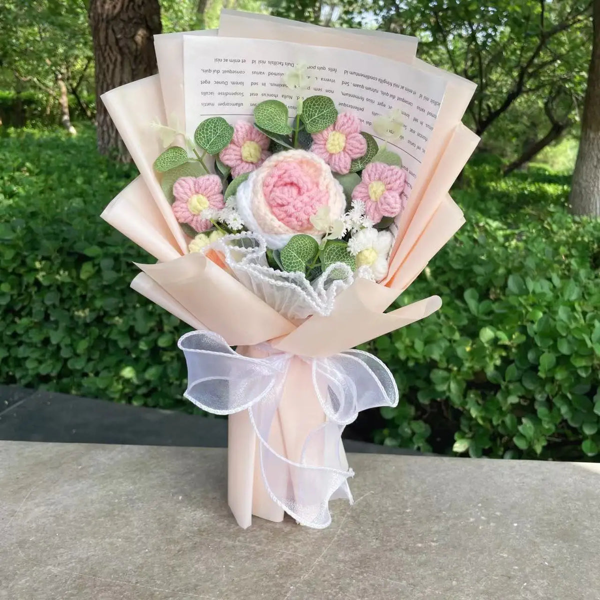 Bouquet aus handgefertigten Häkelblumen in rosa und weiß, umwickelt mit durchscheinendem Band und präsentiert in einem hellro
