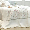 White quilted bedspread featuring delicate embroidered floral vines in soft pinks and greens.