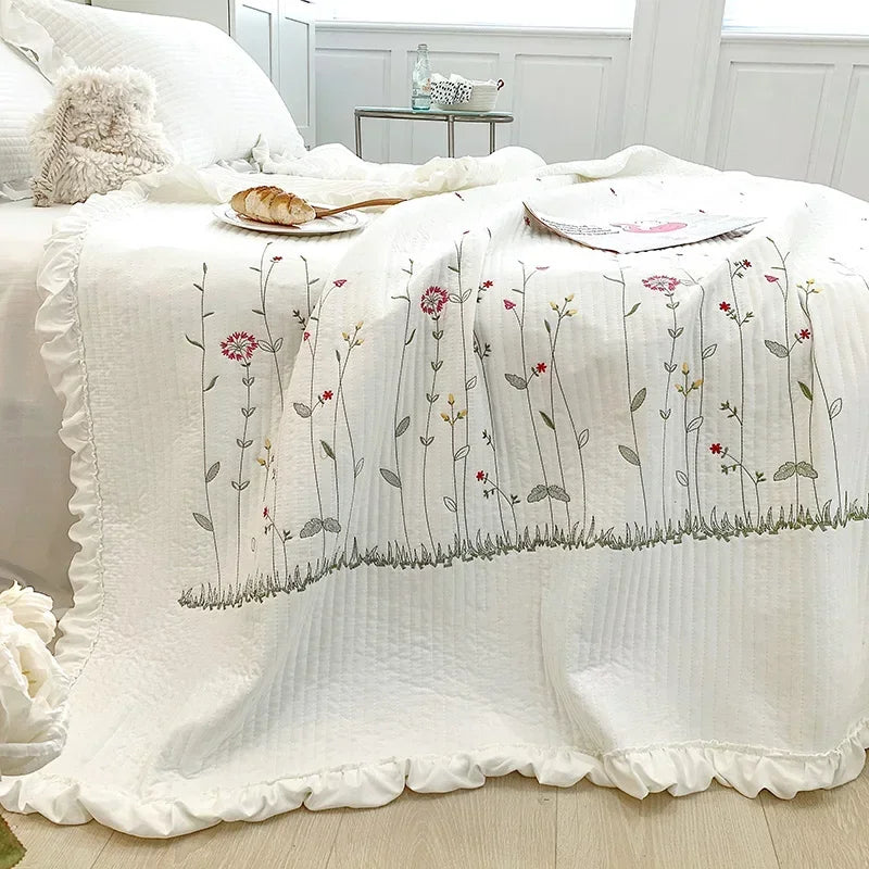 White quilted bedspread featuring delicate embroidered floral vines in soft pinks and greens.