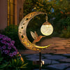A golden crescent moon light fixture featuring a silhouette of a bird in flight, set outdoors.
