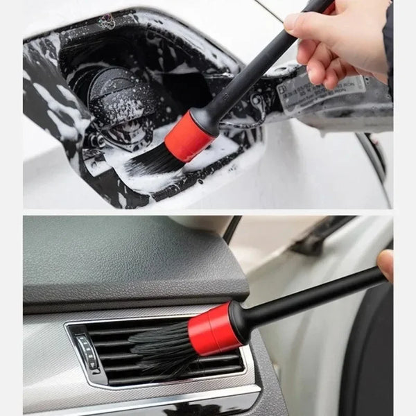 A hand is using a black and red car cleaning brush to detail the interior of a car.
