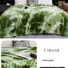 A green and white tie-dye flannel fleece throw blanket draped on a bed.