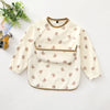 A cream waterproof long-sleeve smock for toddlers with a brown trim and small pink bear print.