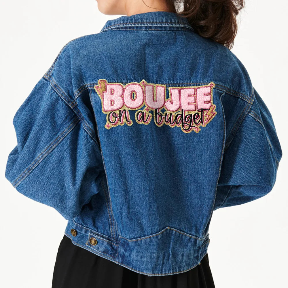 A denim jacket with embroidered text on the back that reads Boujee on a budget