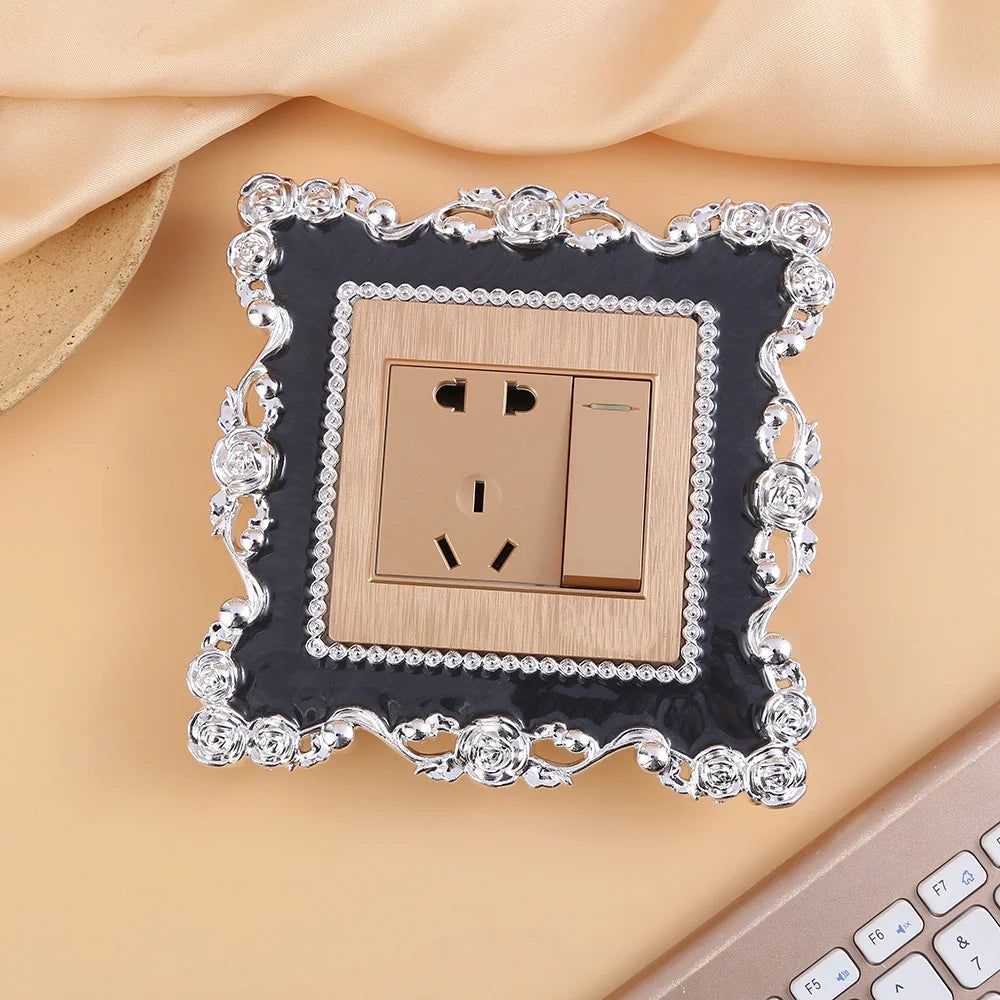 A decorative switch cover frame with a rose pattern border and a brass-toned electrical outlet plate.