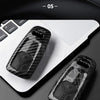 A close-up of a black carbon fiber style key fob cover resting on a white laptop surface.