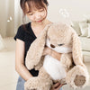A woman is holding a light brown long-eared rabbit plush toy against her chest.
