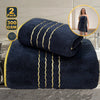 A dark blue luxury bath towel set with gold accents is displayed on a surface, next to a woman wearing a similar towel.