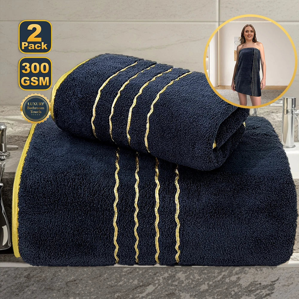 A dark blue luxury bath towel set with gold accents is displayed on a surface, next to a woman wearing a similar towel.