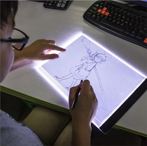 A person is using a transparent LED tracing light to draw on paper with a pen.