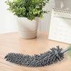 A gray microfiber duster is shown lying on a wooden surface, demonstrating electrostatic adsorption for cleaning.