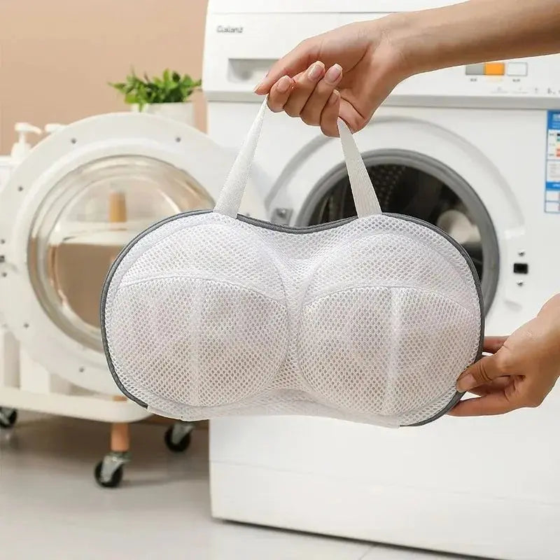 A hand is holding a white fine mesh laundry bag for delicate underwear near a washing machine.