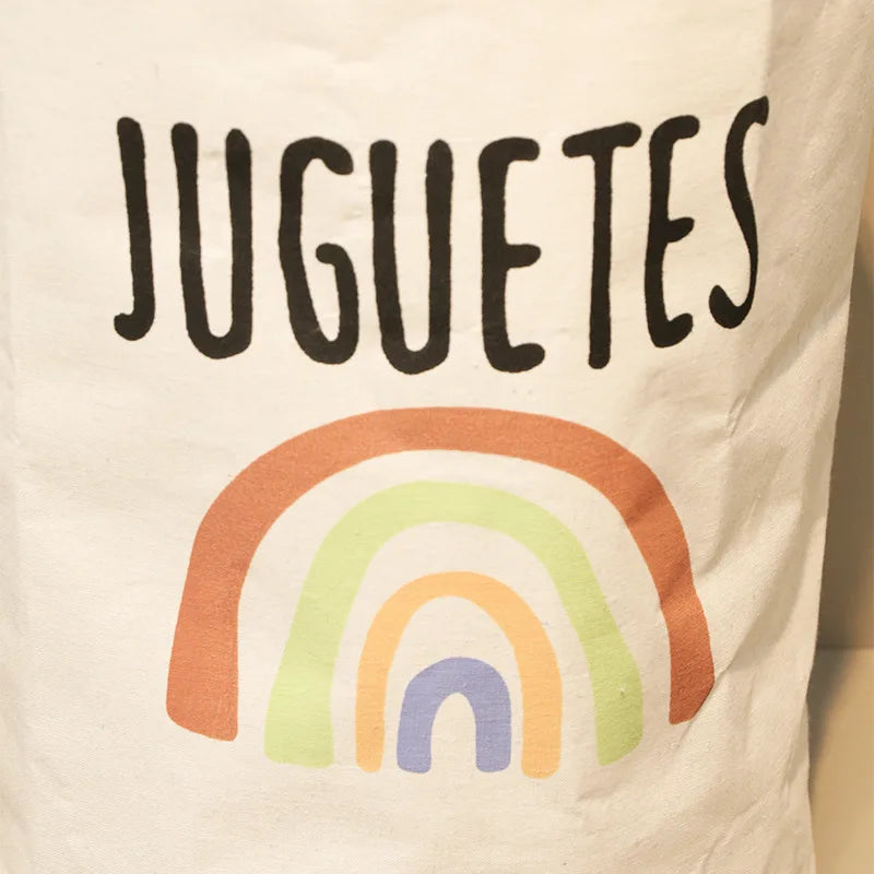 A white fabric featuring the text JUGUETES and a colorful rainbow design.