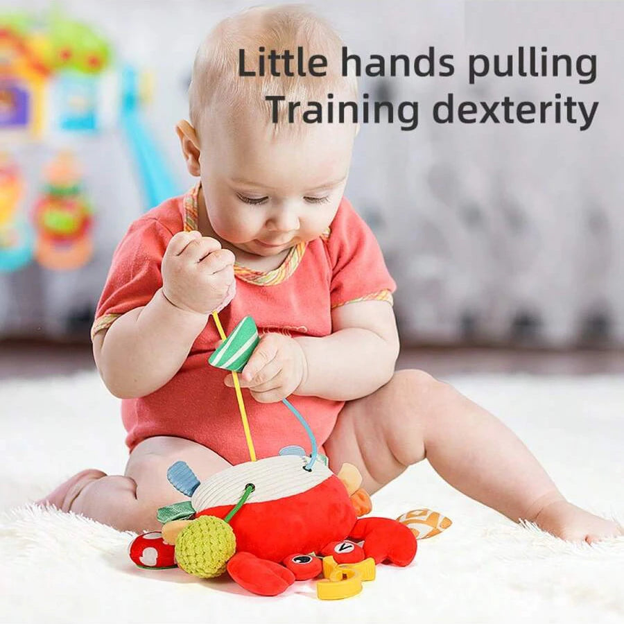 A baby is using a hanging rattle and teether toy with a cartoon pendant to practice dexterity.