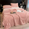 A thick pink flannel blanket with ribbed texture is displayed on a bed, featuring matching pillows and a decorative tray.