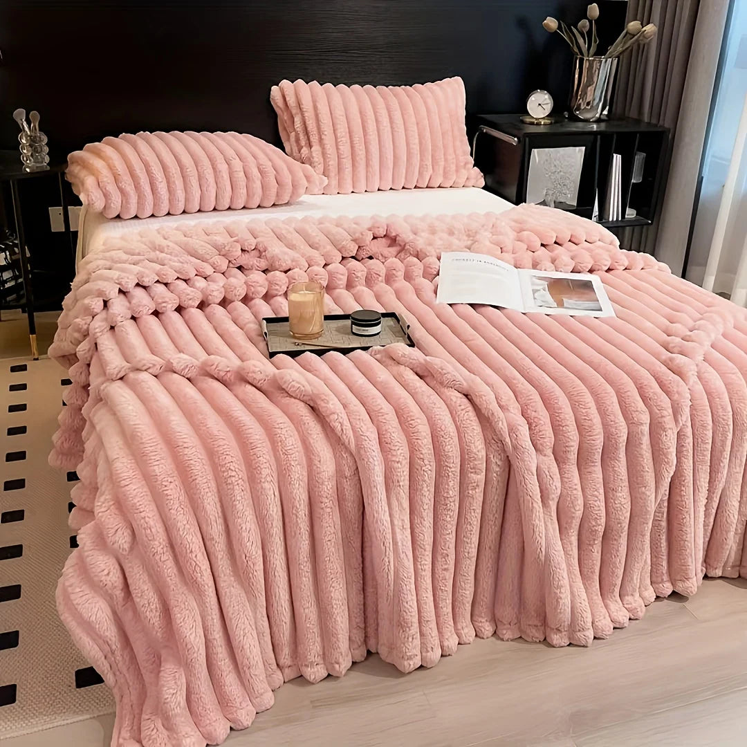 A thick pink flannel blanket with ribbed texture is displayed on a bed, featuring matching pillows and a decorative tray.